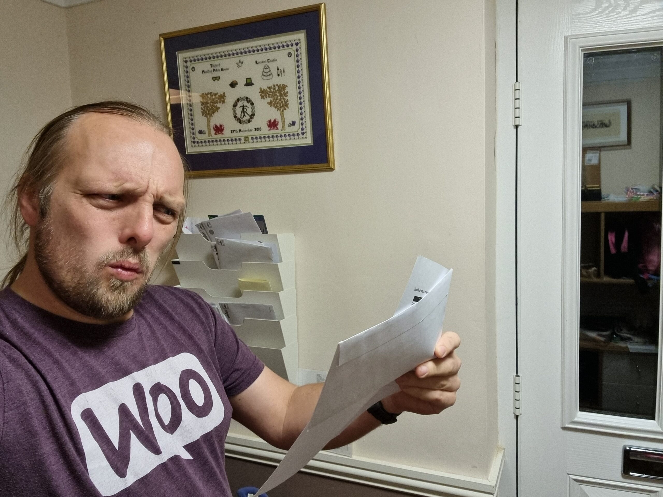 Full image of Dan, near his front door, reads his mail. His facial expression suggests that he's about to exclaim "What!?"