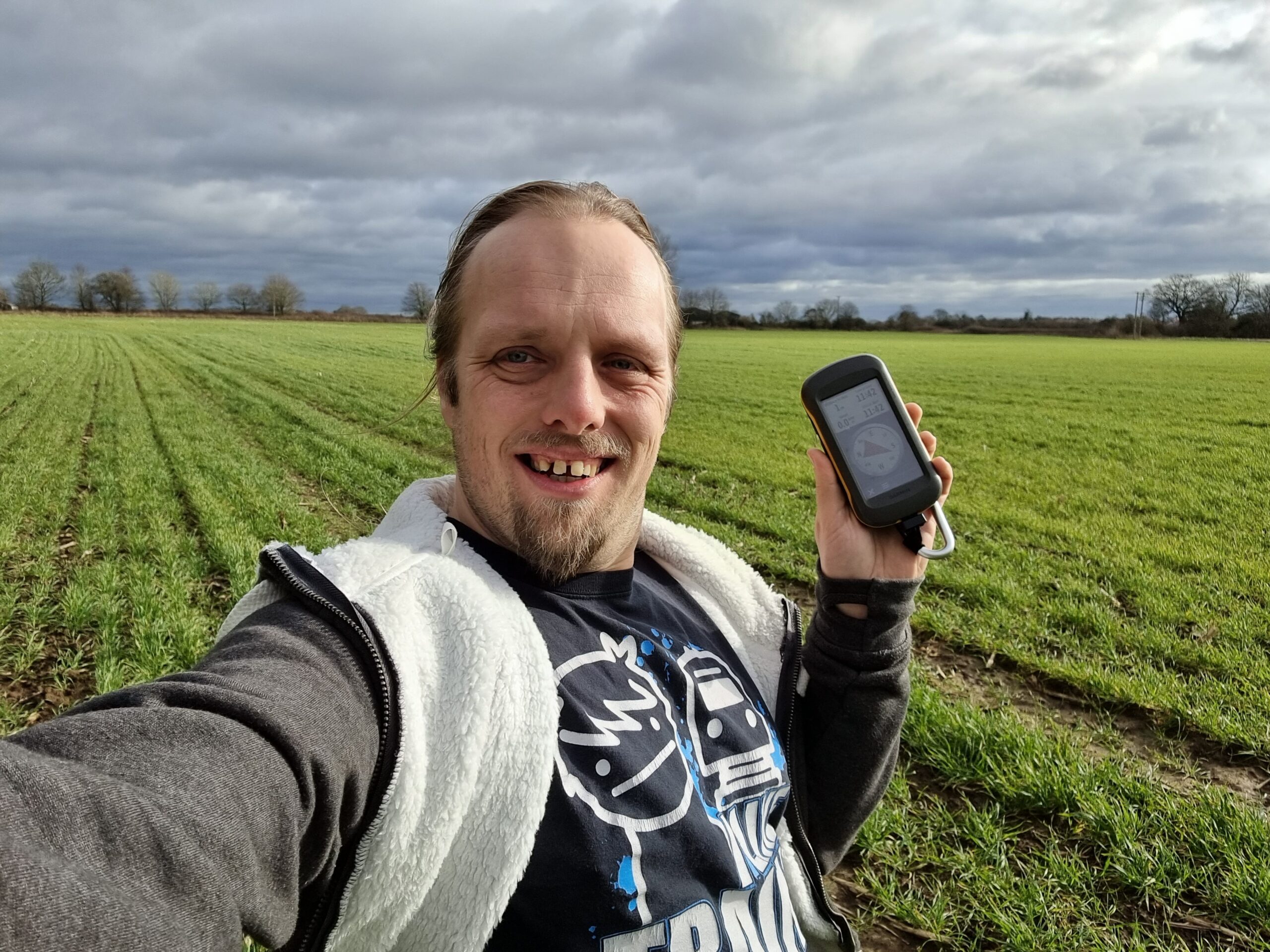 Full image of Dan in a grassy field holding a GPSr and grinning