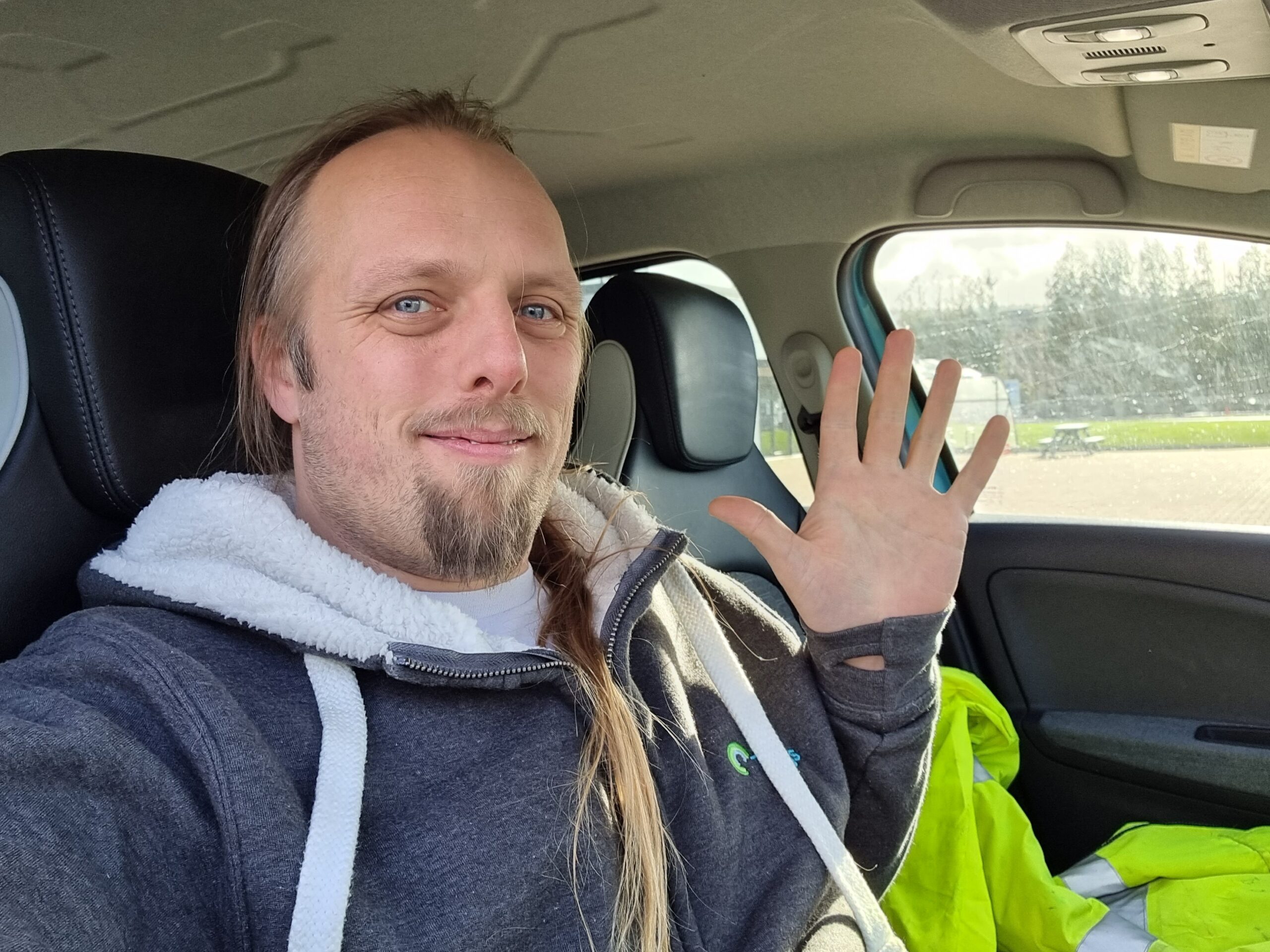 Full image of Dan waving, sat in a car.