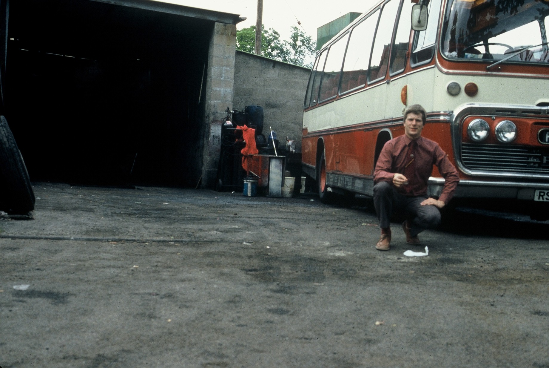 Full image of Dan's dad crouches next to a bus in a somewhat lopsided-photo.