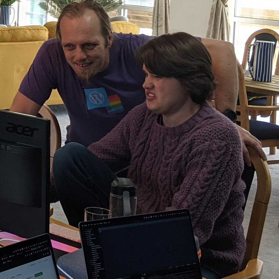 Full image of Dan and Jacob look at a piece of code together; Dan is smiling but Jacob looks disgusted.