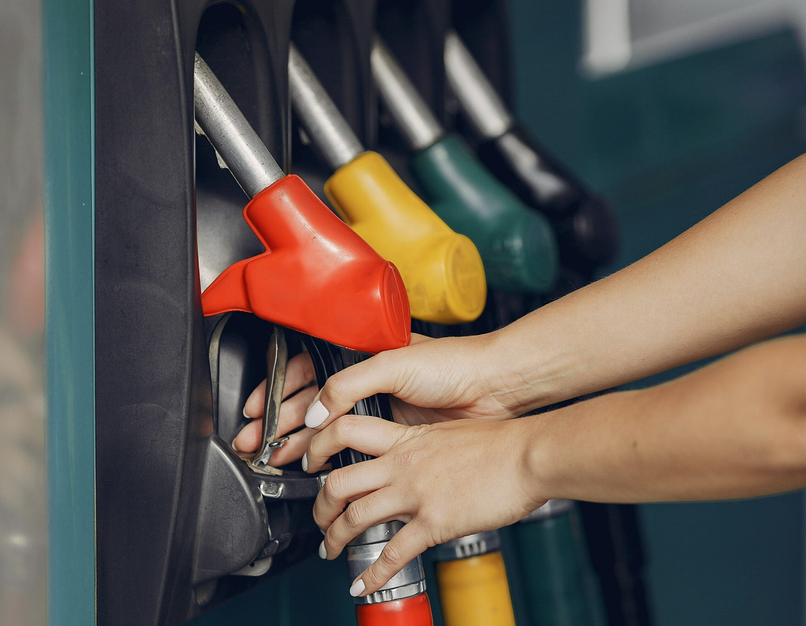 Full image of A woman's hand reaches for one of four fuel pump nozzles. Photo by Gustavo Fring, used under the Pexels License.