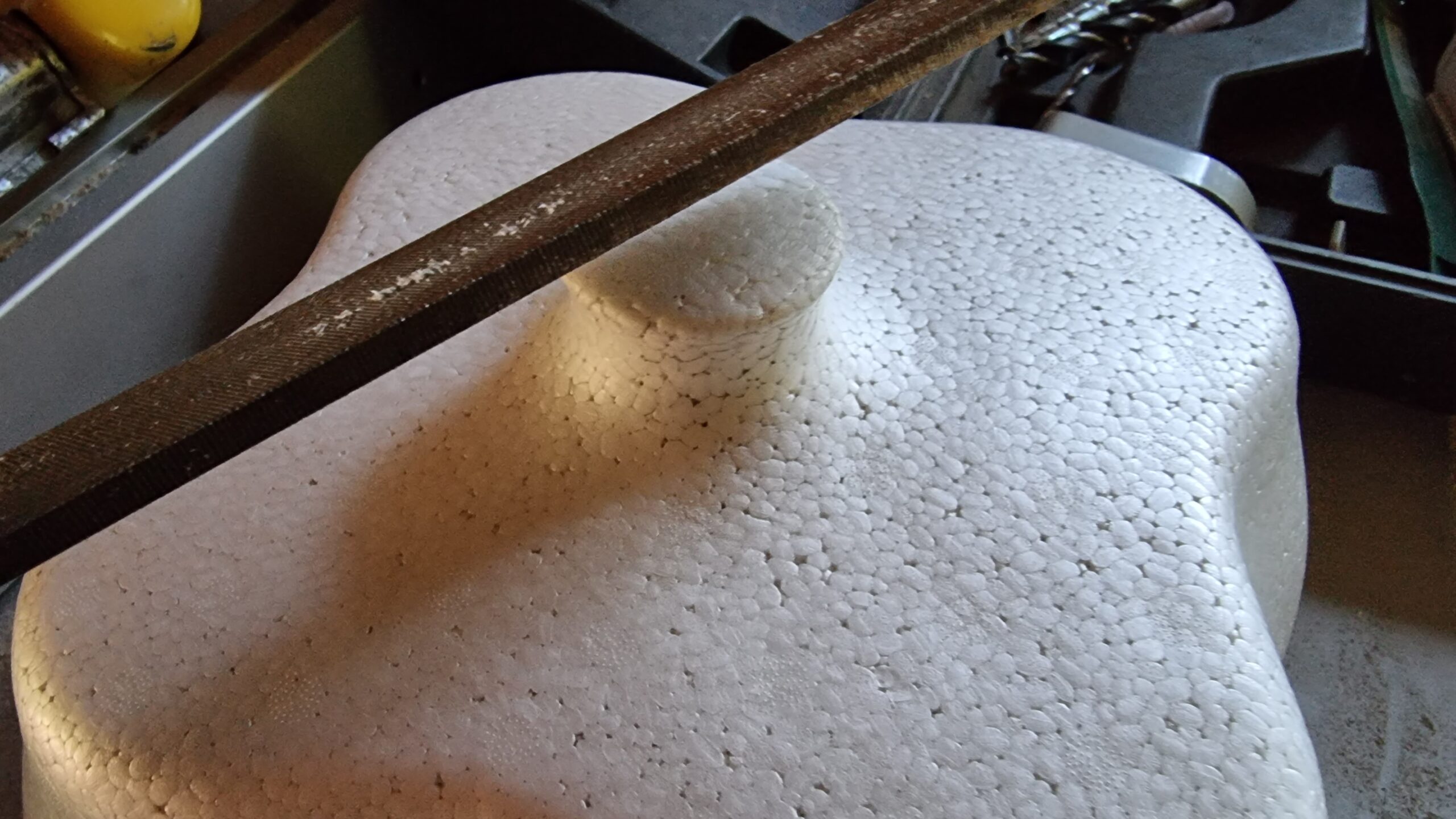 Full image of Top of a reinforced polystyrene doorstep milk storage box, showing the round-topped handle. A metal file sits atop the box, about to be used to file down the handle.