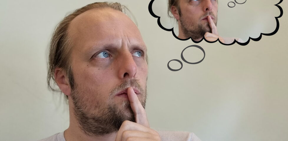 Against a pale background, Dan, deep in thought and with a finger to his lips, staring into space. A stylised thought bubble above him shows that he is thinking about himself thinking about himself thinking about himself, and so on (implied to infinity).