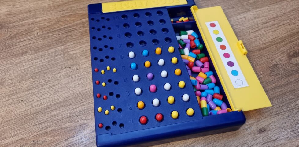 A plastic Mastermind board in blue and yellow with ten guess spaces and eight pegs. The sixth guess is unscored but looks likely to be the valid solution.