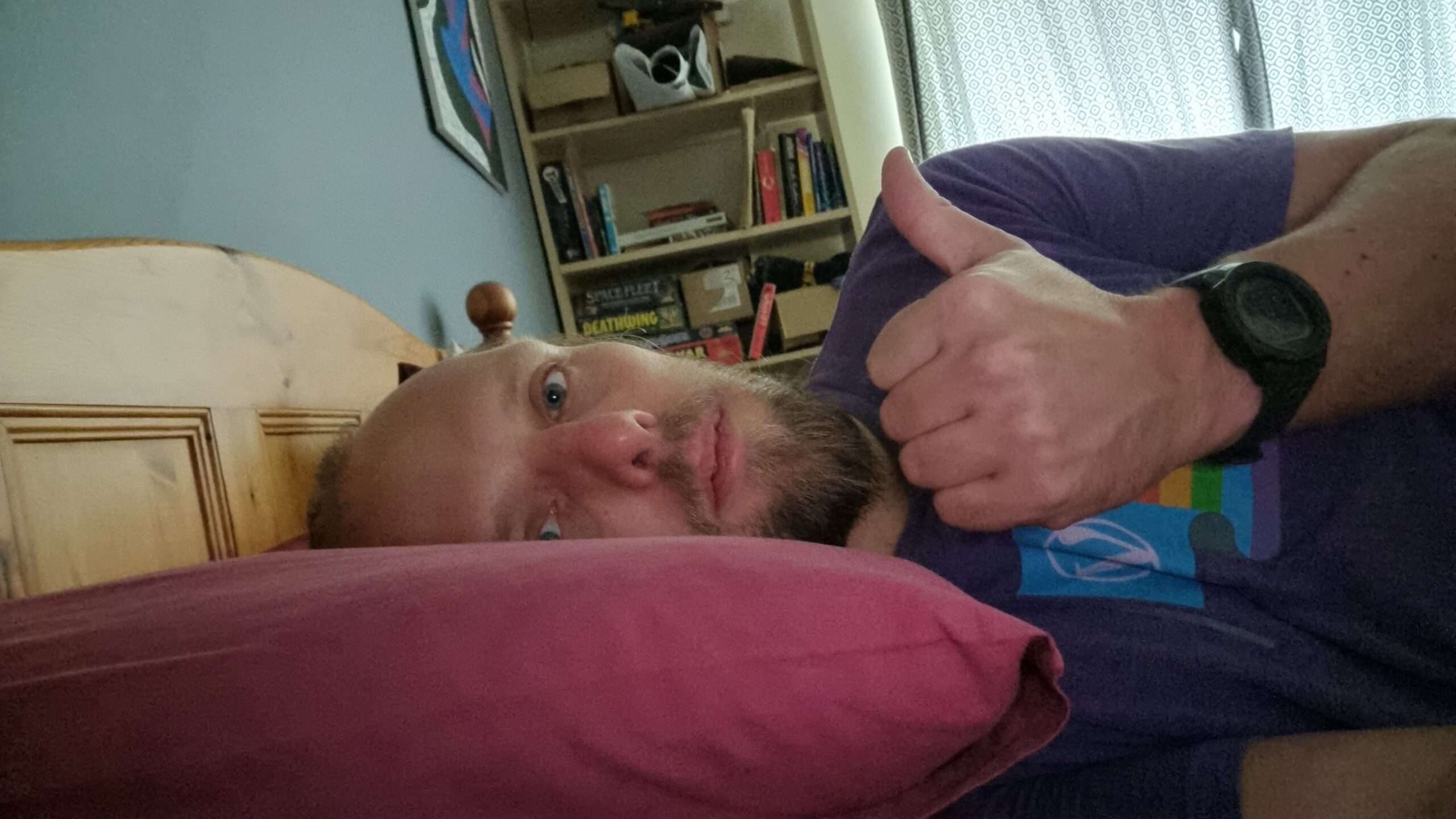 Full image of Dan lying in bed, giving a weak "thumbs up".