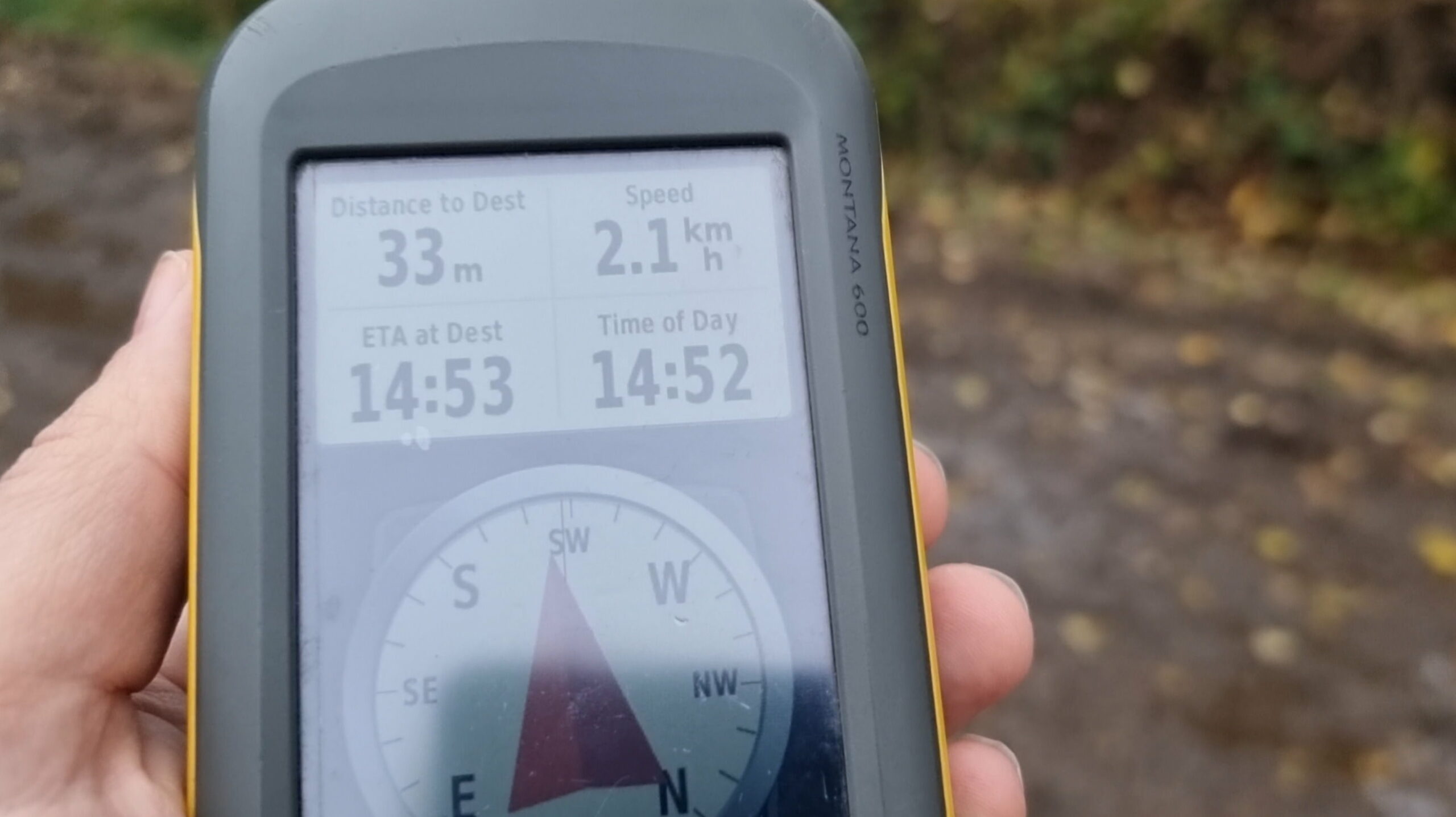 Full image of A GPSr unit, held in Dan's left hand, shows 33 metres to a destination, straight ahead. In the background the edge of the farm lane can be made out in that direction.