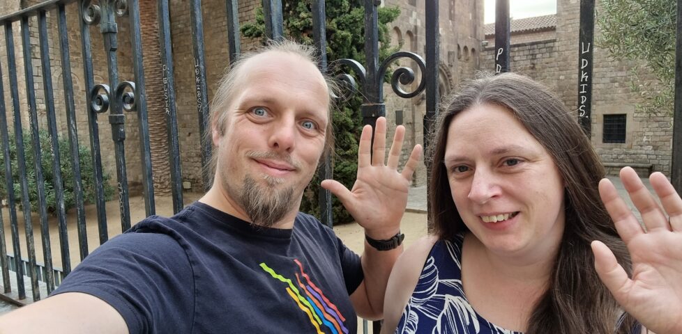 Dan and Ruth in front of a monastary gates, smiling and waving.