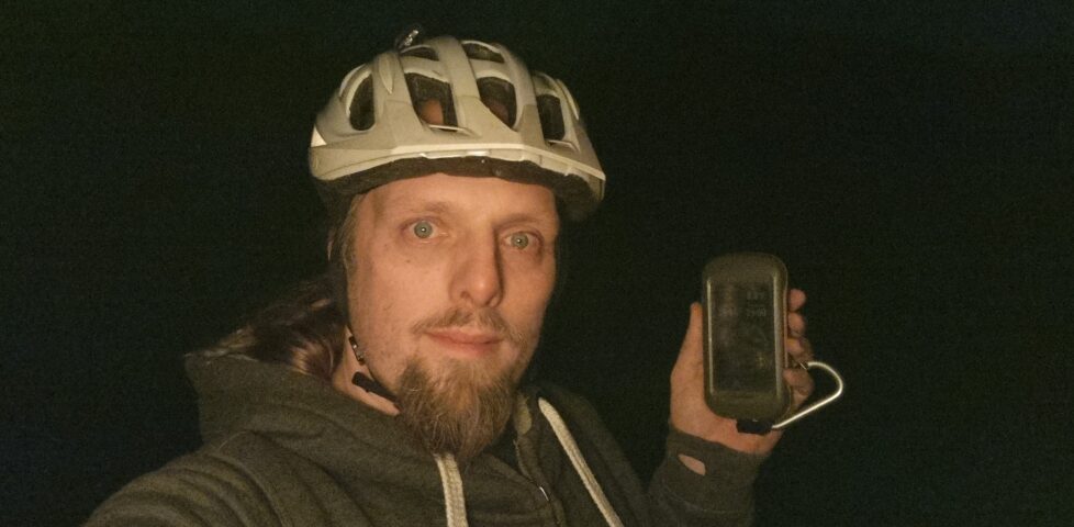 Dan, in the dark and wearing a cycle helmet, holds up a GPS receiver.