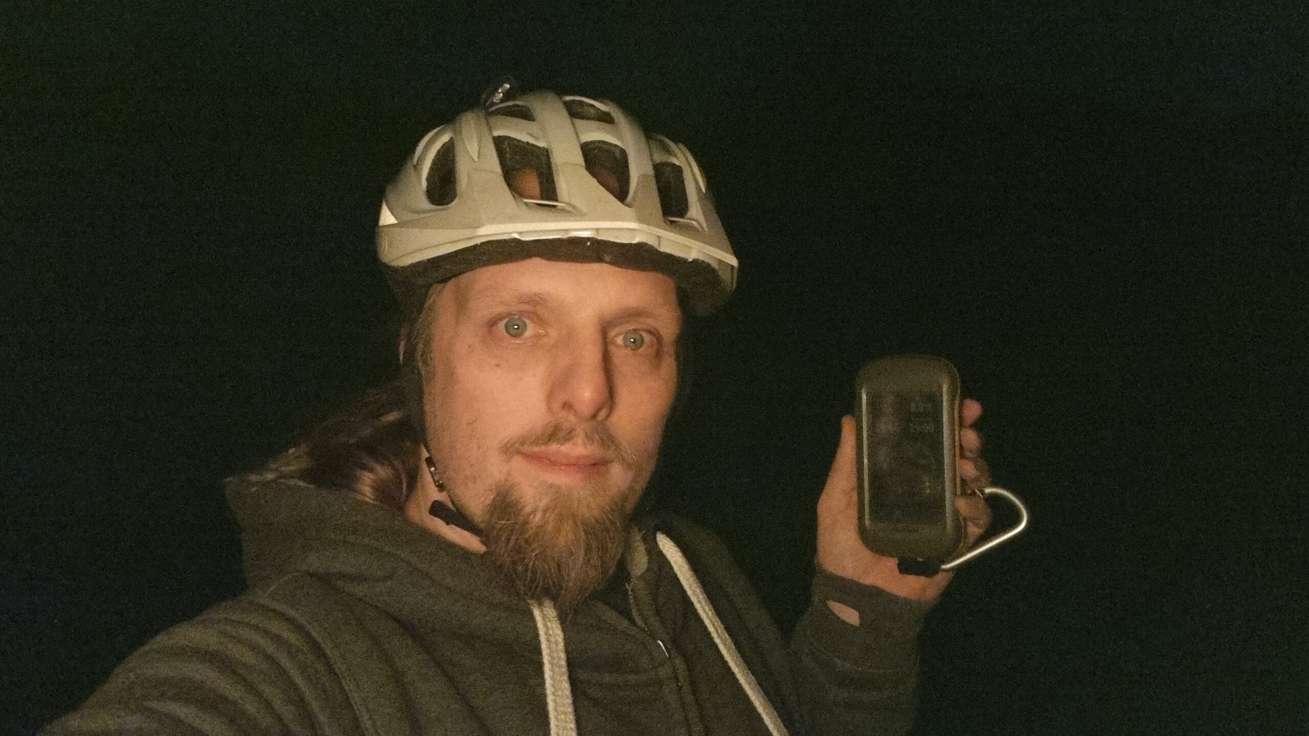 Full image of Dan, in the dark and wearing a cycle helmet, holds up a GPS receiver.