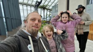 In an enclosed garden atop a skyscraper, Dan and two children smile for the camera.