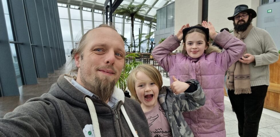 In an enclosed garden atop a skyscraper, Dan and two children smile for the camera.