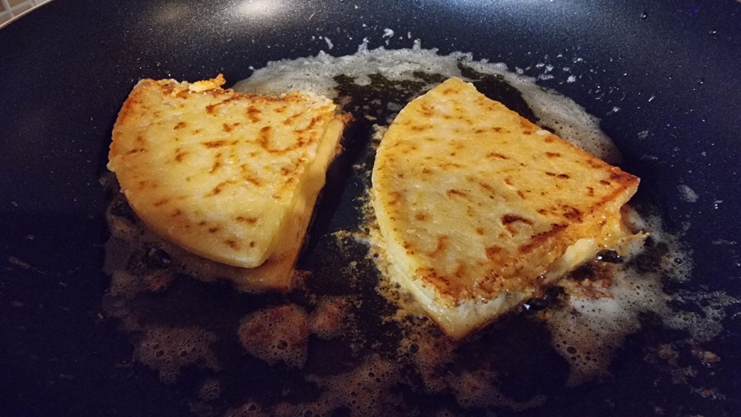 Full image of A pair of tattie scone quesadillas sizzling in a pan.