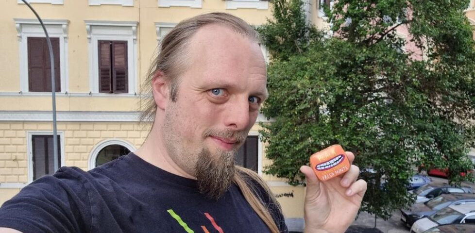 Dan holding an orange mint tin in a city centre.