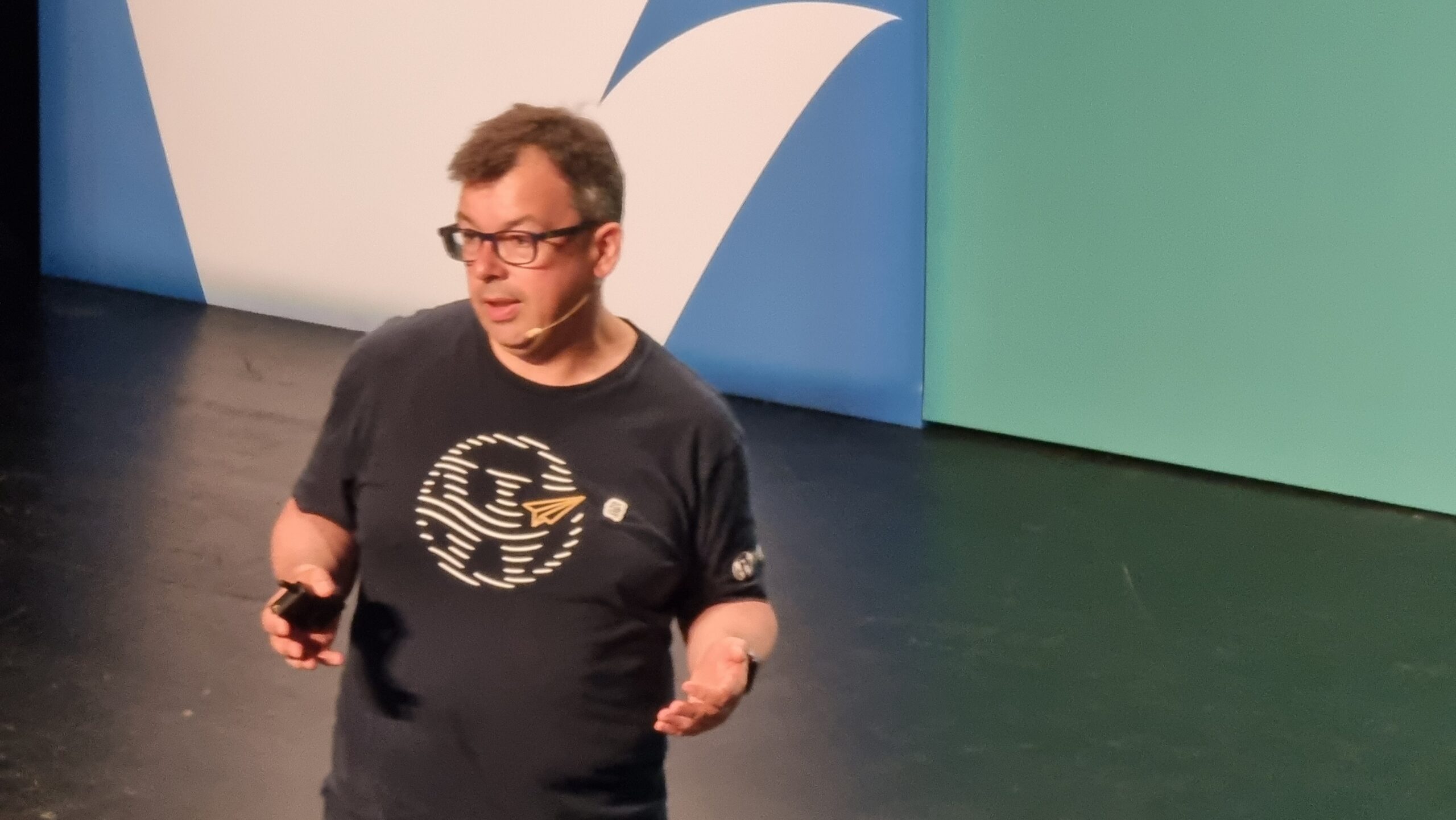 Full image of A man wearing glasses and a t-shirt with a WordPress logo stands on a stage.