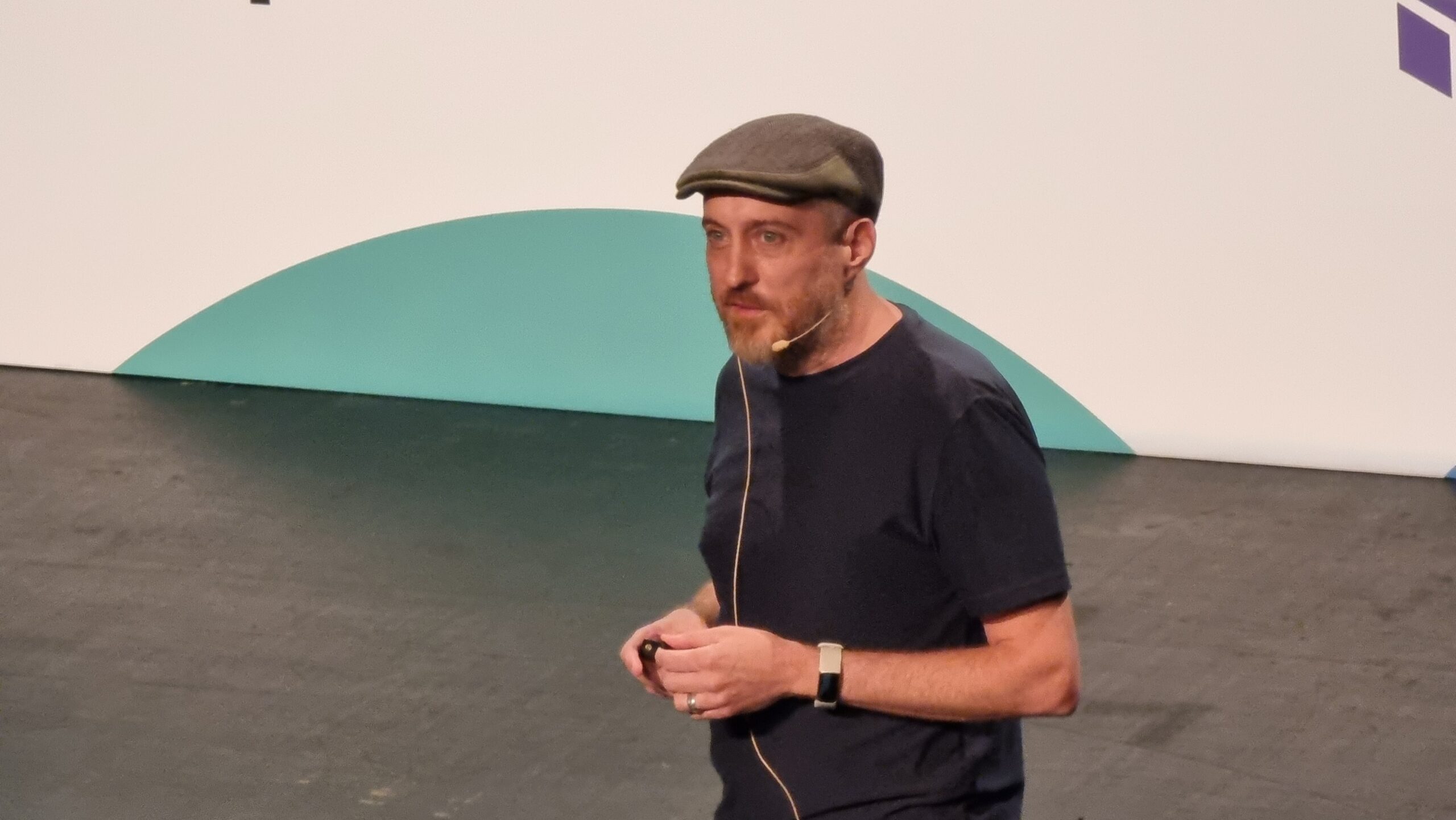 Full image of A man wearing a flat cap strides across a stage.
