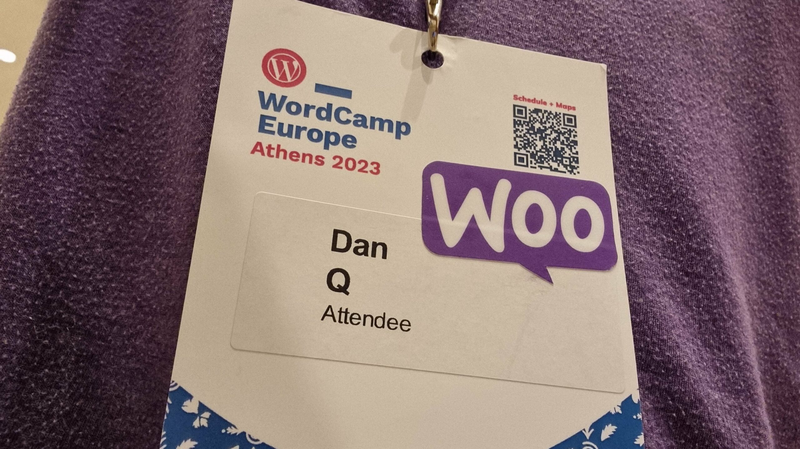 Full image of A WordCamp Europe Athens 2023 lanyard and name badge for Dan Q, Attendee, onto which a "Woo" sticker has been affixed.