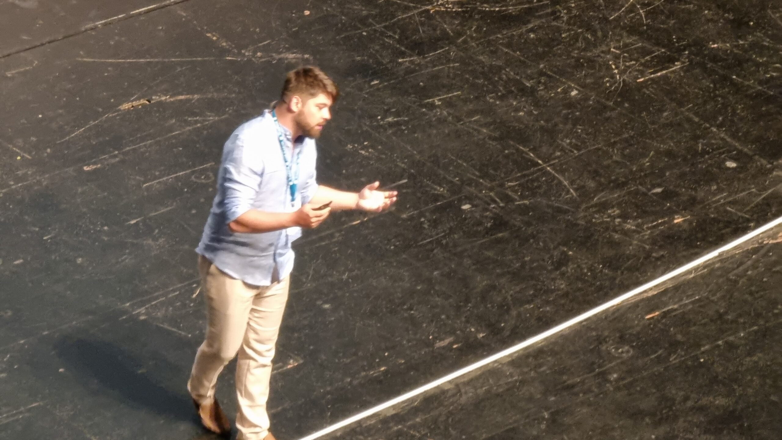 Full image of A man in a blue shirt stands on a large stage.
