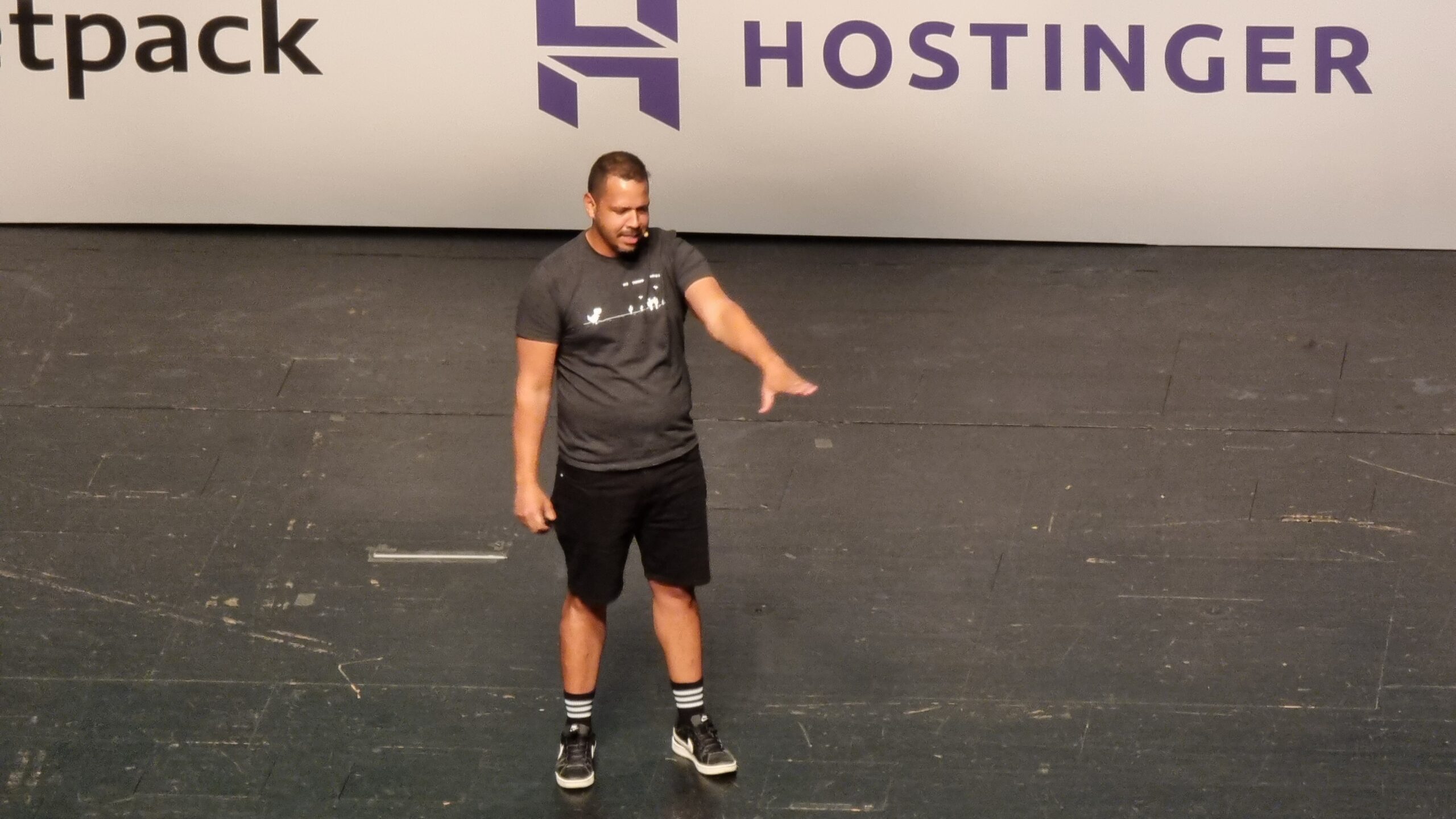 Full image of A man on a stage with his arm out in greeting to the crowd in front of him.
