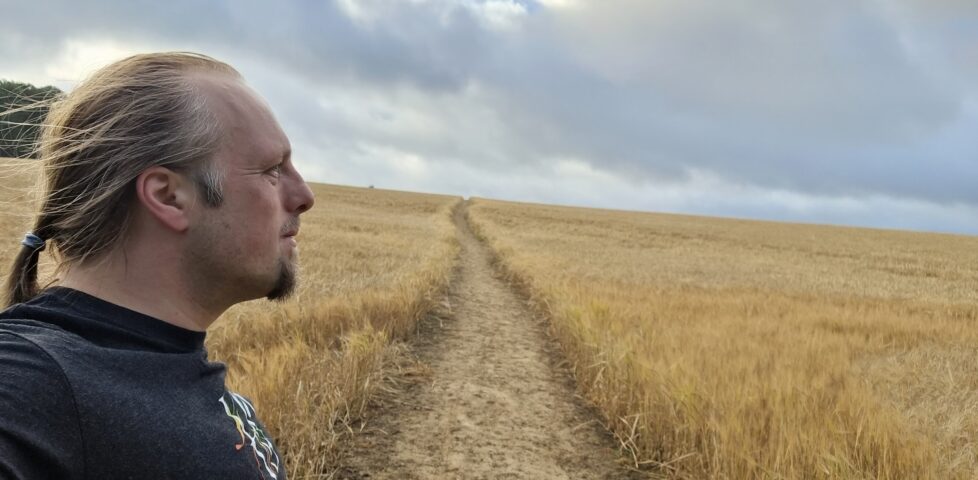 Dan, on a path through a young cornfield, stares towards the distant clouds.