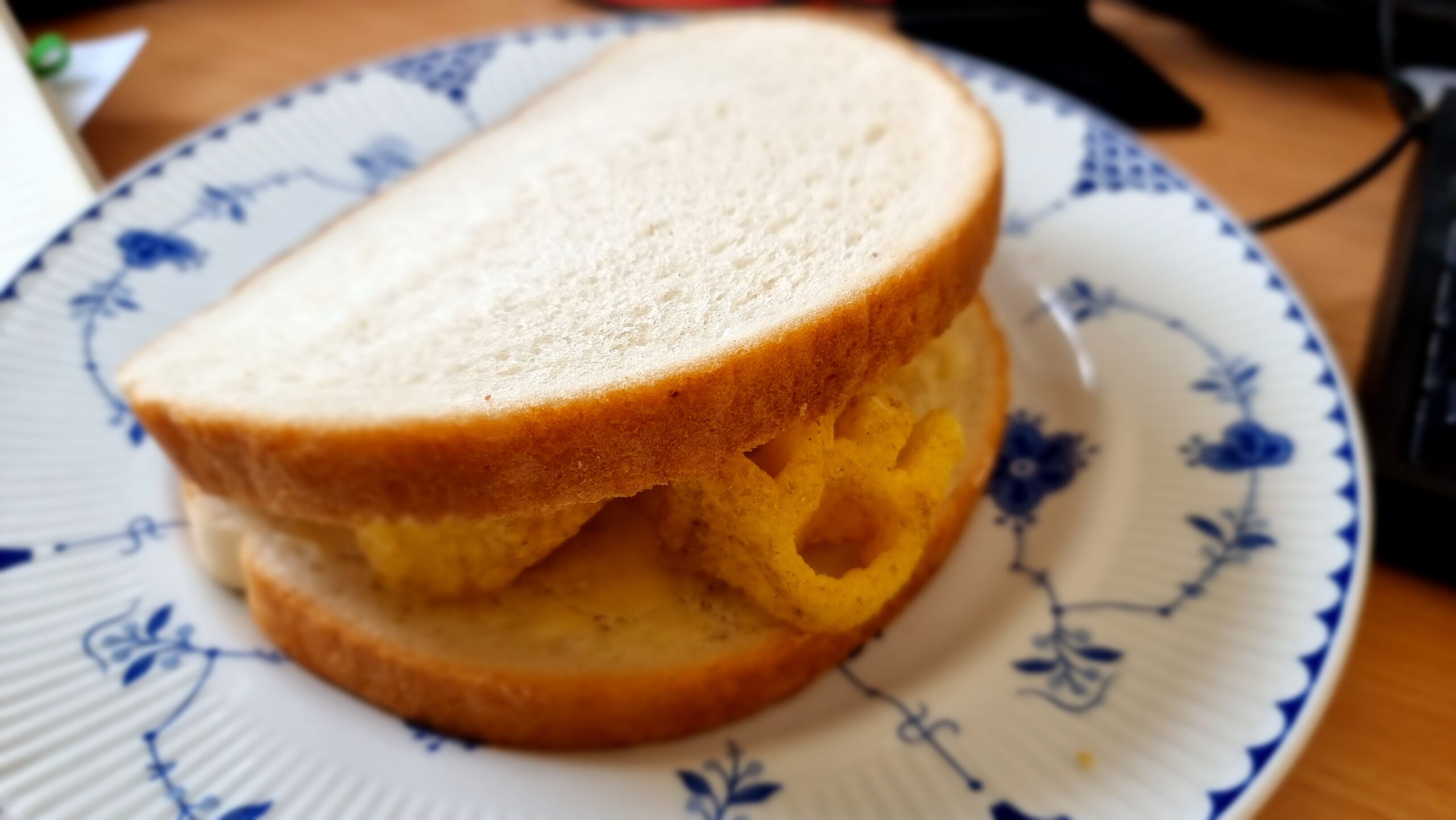Full image of Thich white sandwich on a blue-and-white china plate, with the distinctive shape of an organge-coloured Monster Munch crisp poking out.
