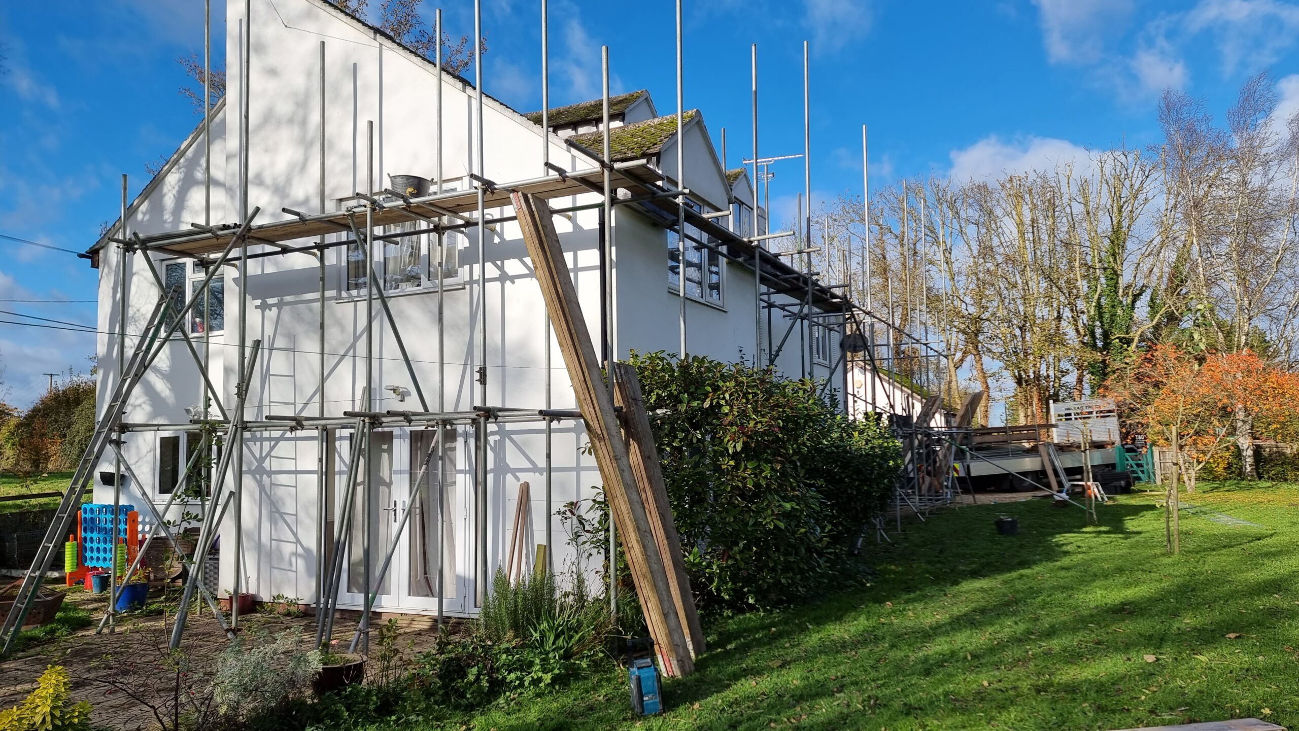Full image of Photograph showing a detached white house clad in scaffolding, under a clear blue sky.