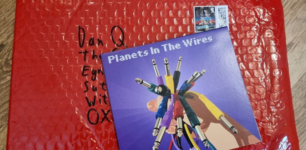 Slim CD case of the album atop a padded envelope made of red bubble wrap.