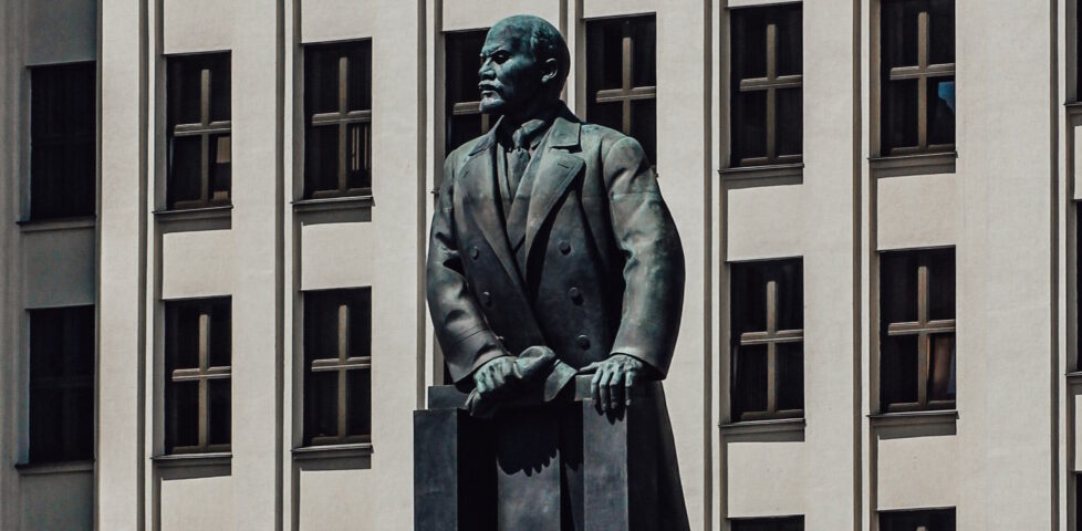 Photograph of the Statue of Lenin in Independence Square, Minsk: Government House #1 stands behind a large metal statue of Vladimir Lenin, looking to his right/