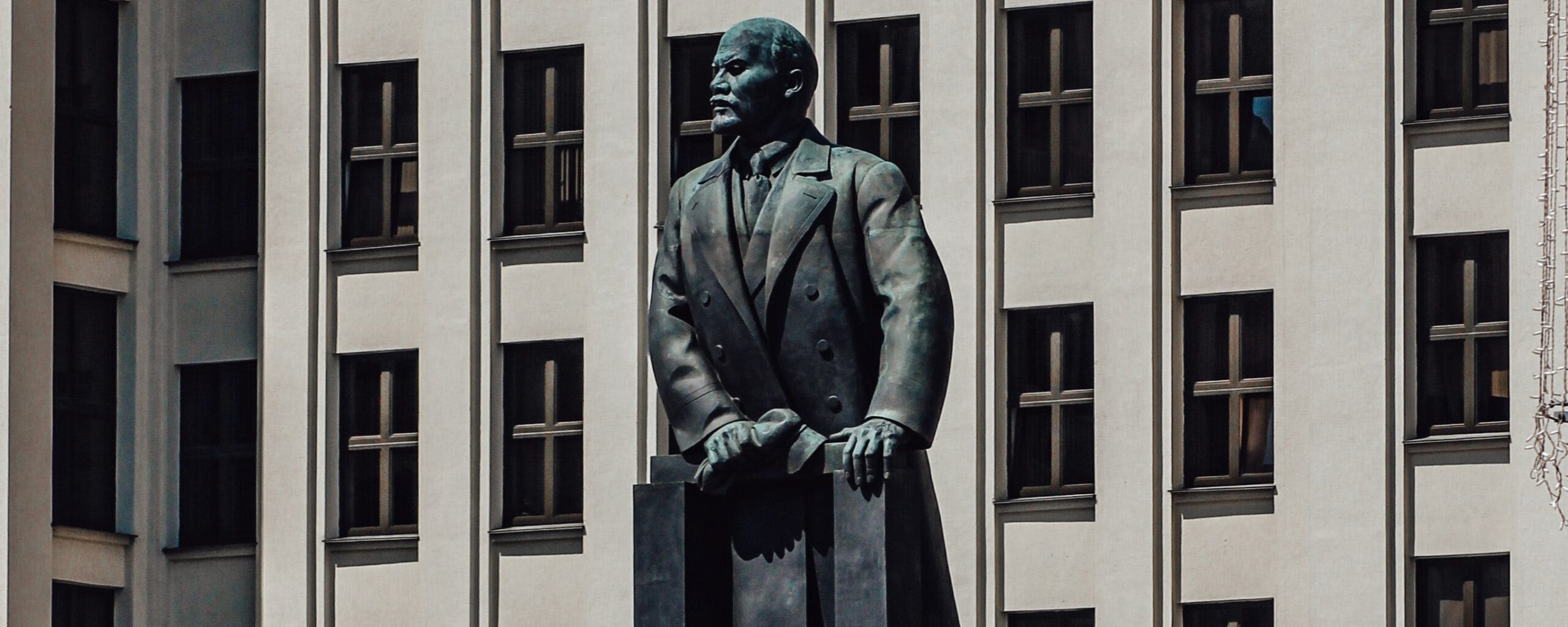 Full image of Photograph of the Statue of Lenin in Independence Square, Minsk: Government House #1 stands behind a large metal statue of Vladimir Lenin, looking to his right.