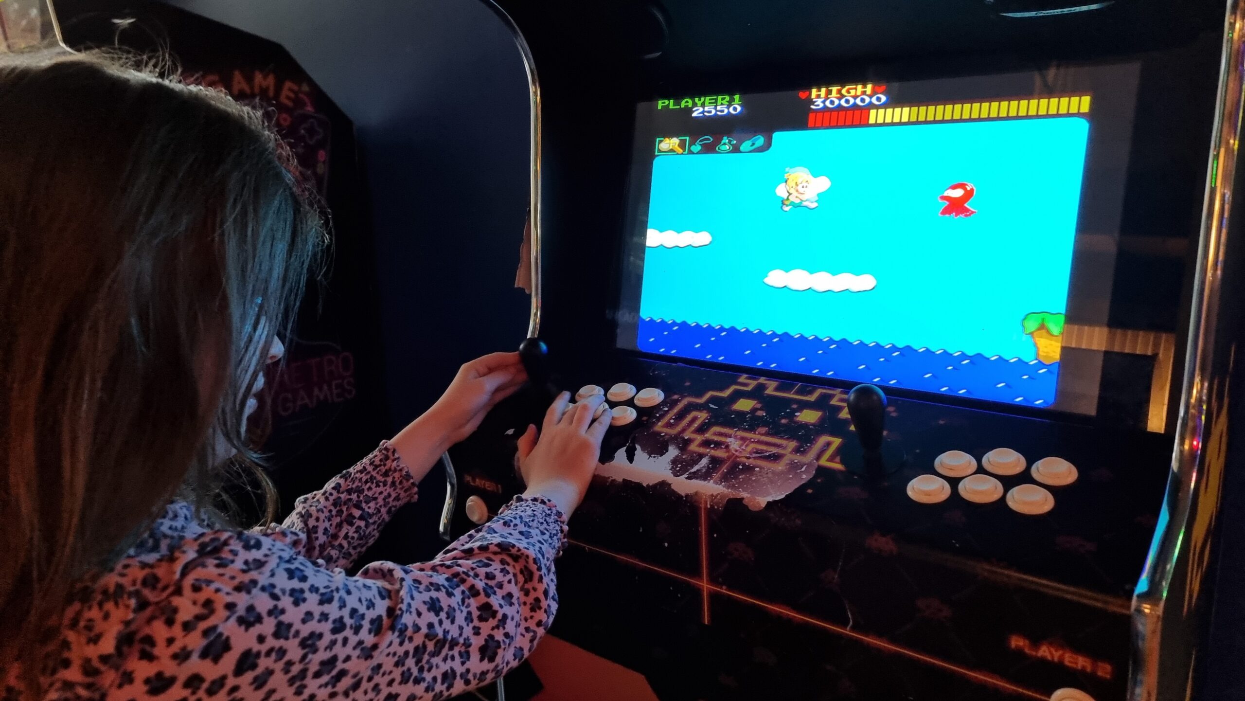 Full image of A young girl in a pink leopard-print top plays Wonder Boy on an arcade cabinet.