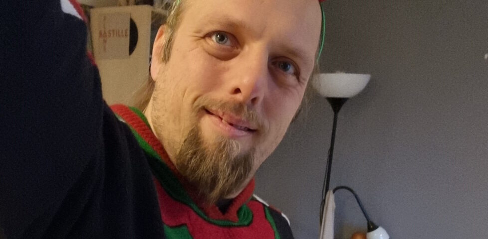 Selfie of Dan wearing an "elf costume" Christmas jumper and matching hat with bell.