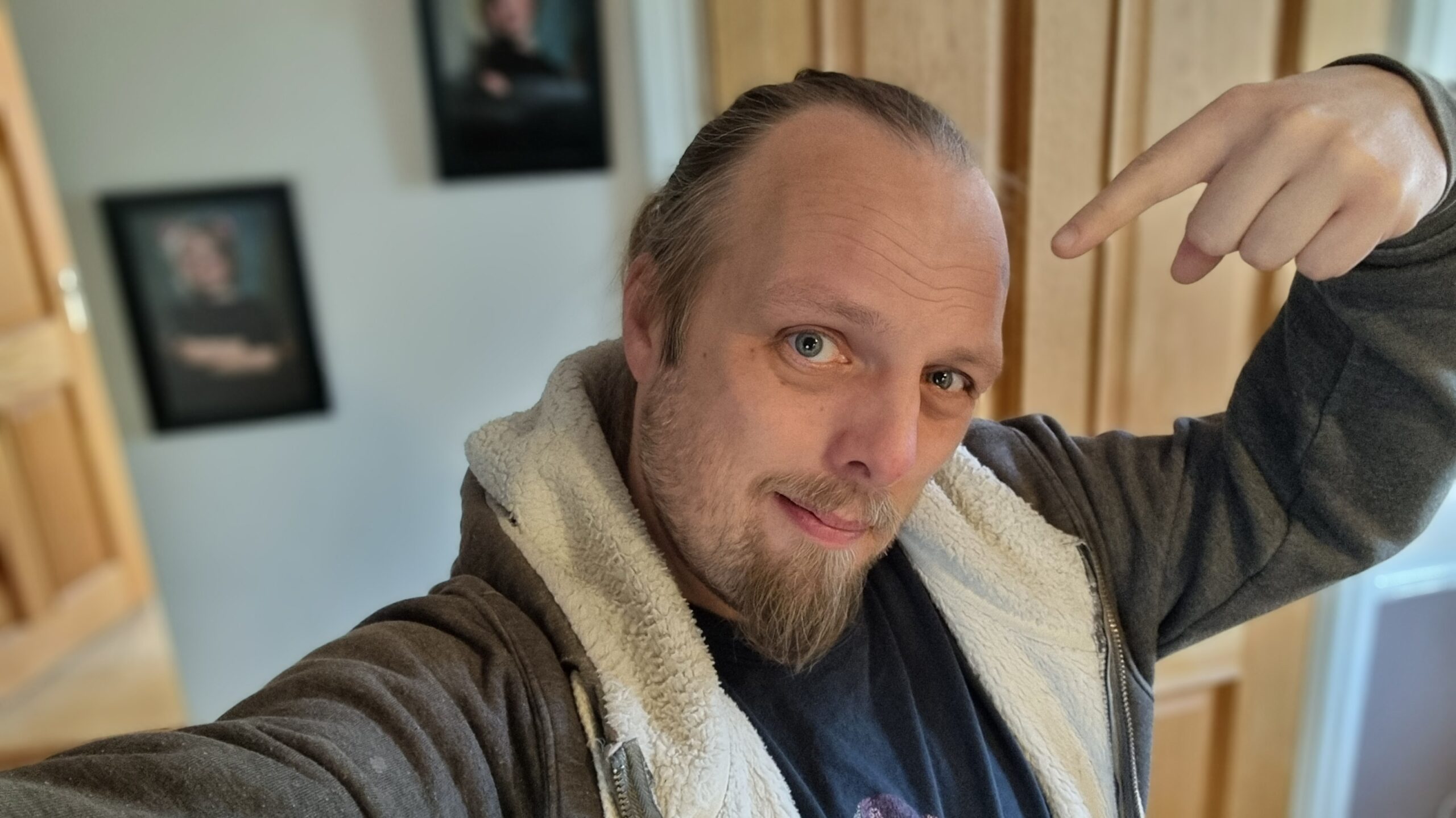 Full image of Dan, a wry smile on his face, pointing at his own head.