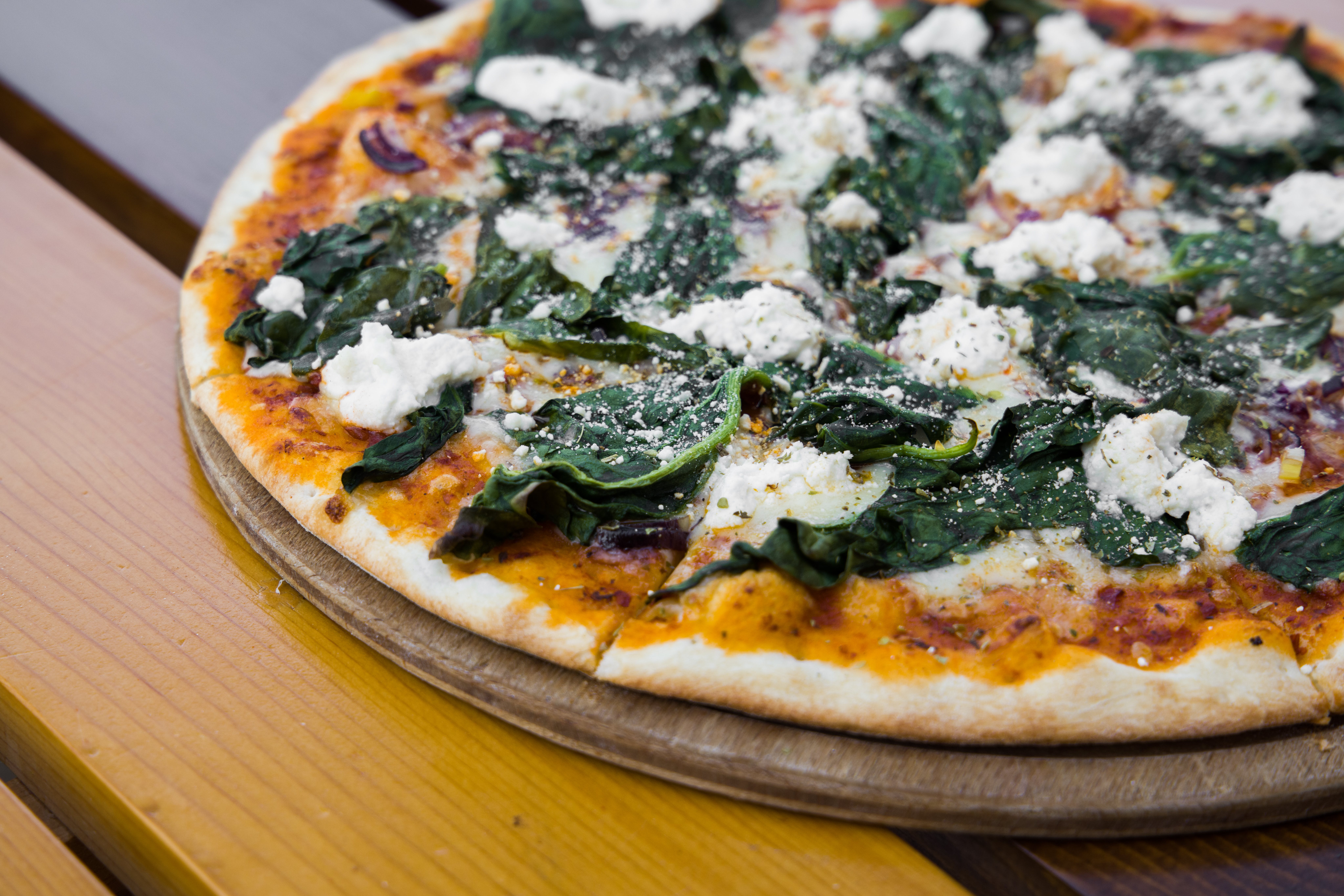 Full image of Freshly-baked pizza with spinach and mushrooms, whole, on a wooden board.
