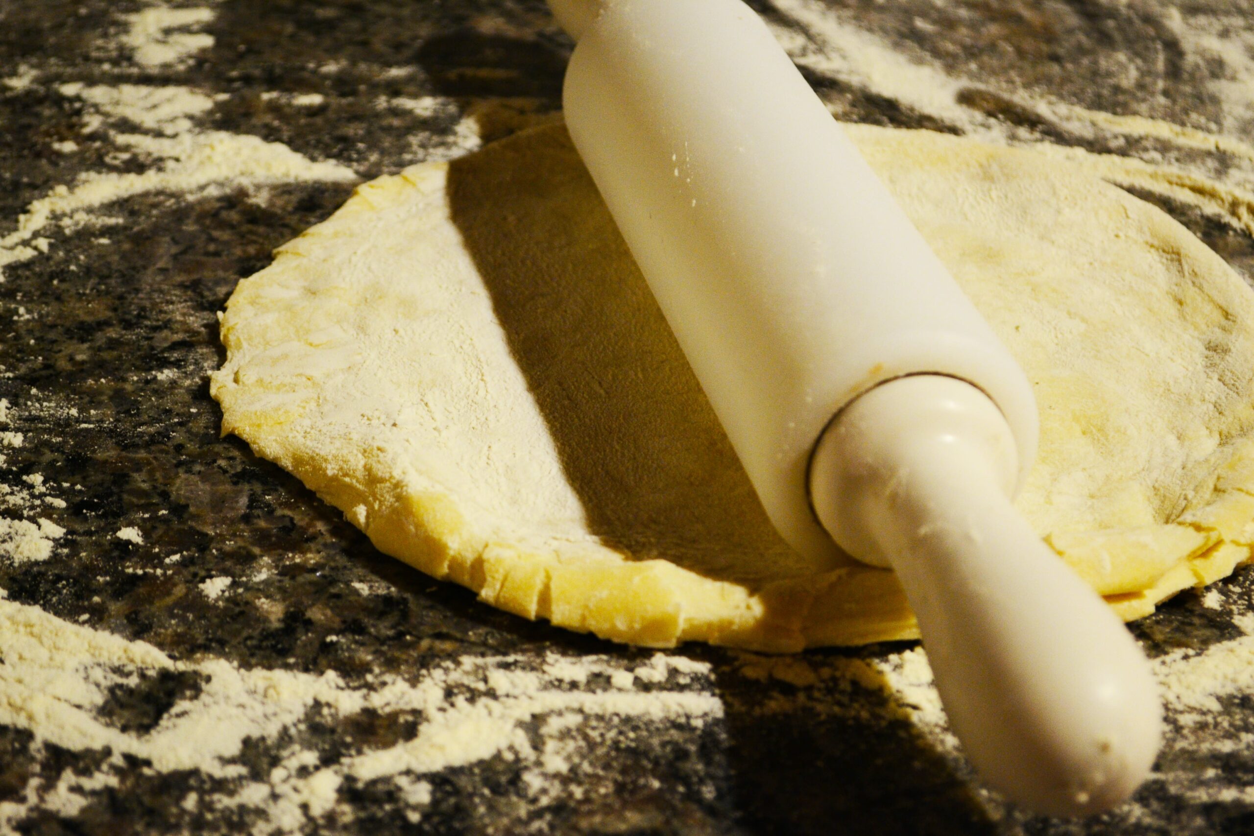 Full image of A circle of pizza dough on a worktop, a rolling pin atop it.