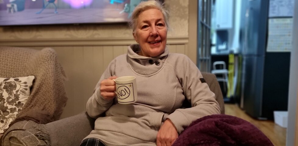 A white-haired woman sitting on a comfortable chair holding a mug.