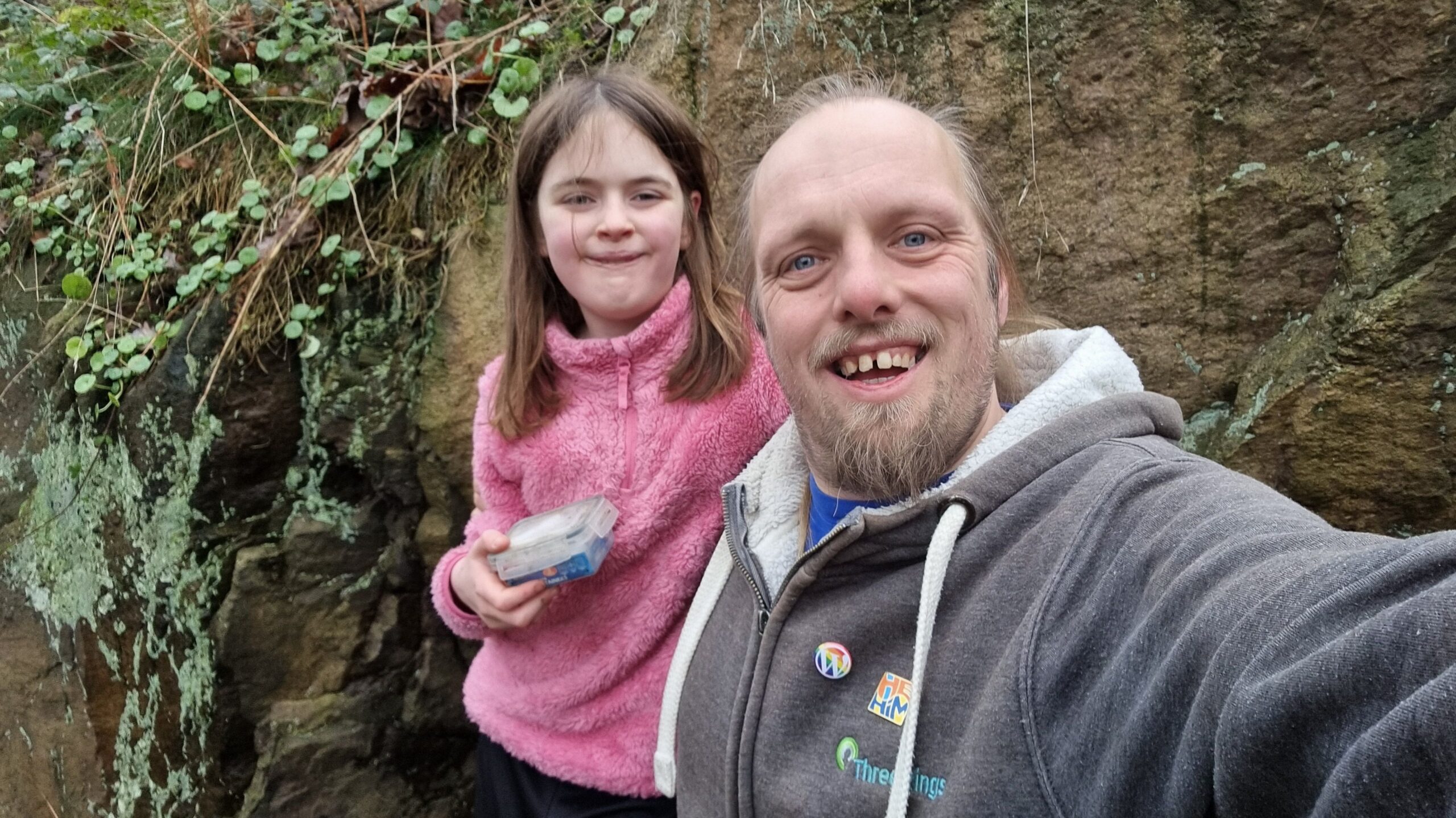 Full image of Dan smiles alongside a 10-year-old girl who's holding a geocache container.