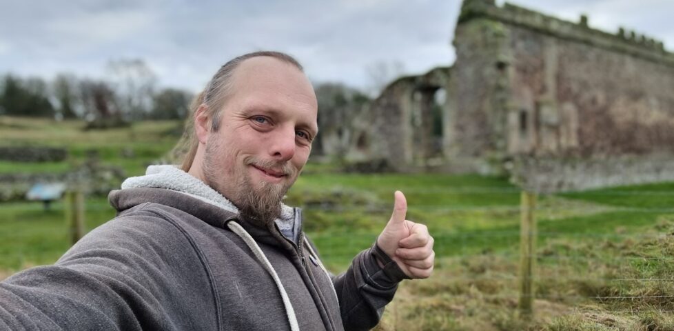 Dan, with his thumb up, in front of the ruin of an abbey.