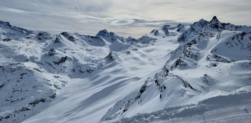 A snow-covered Alpine glacier sandwiched into a gully of exposed rocks.