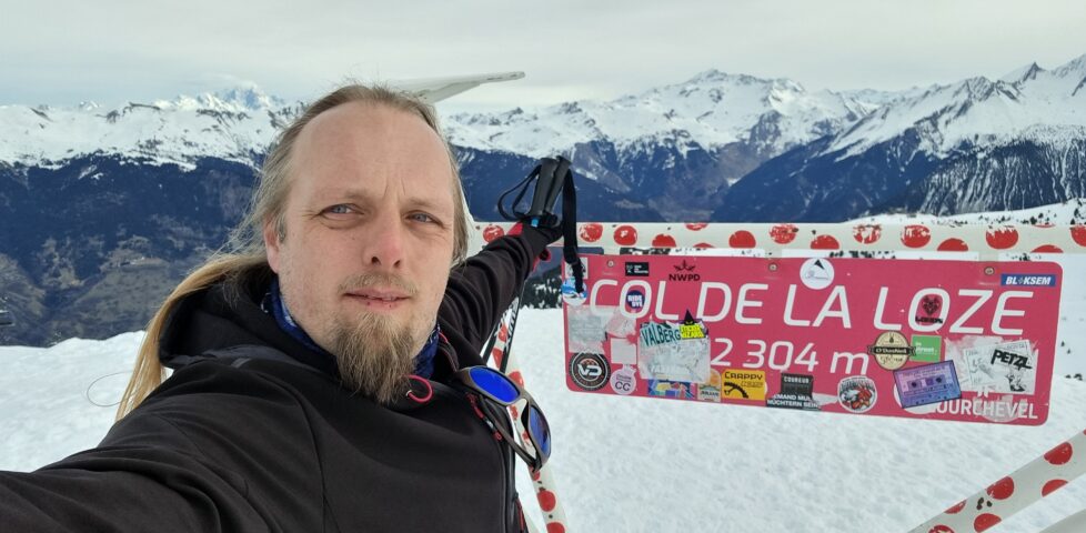 Dan, in a wintery mountainous landscape, poses for a selfie by a sculpture of a bicycle marking part of the route of the Tour de France.