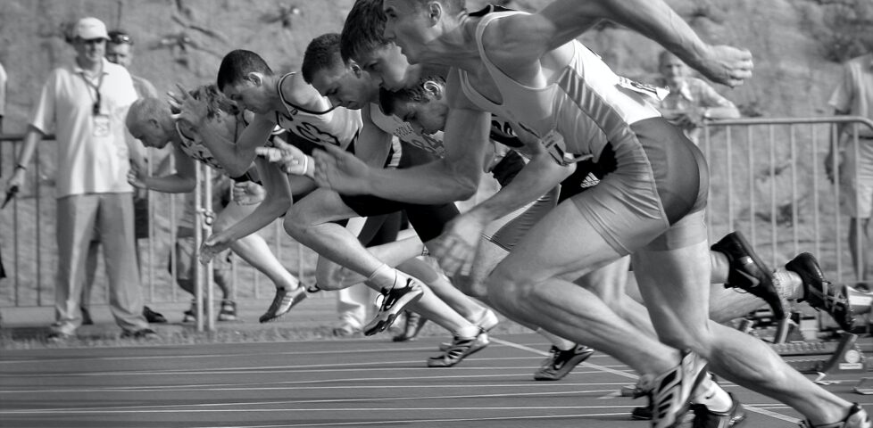 Monochrome photograph showing sprinters at the starting line.