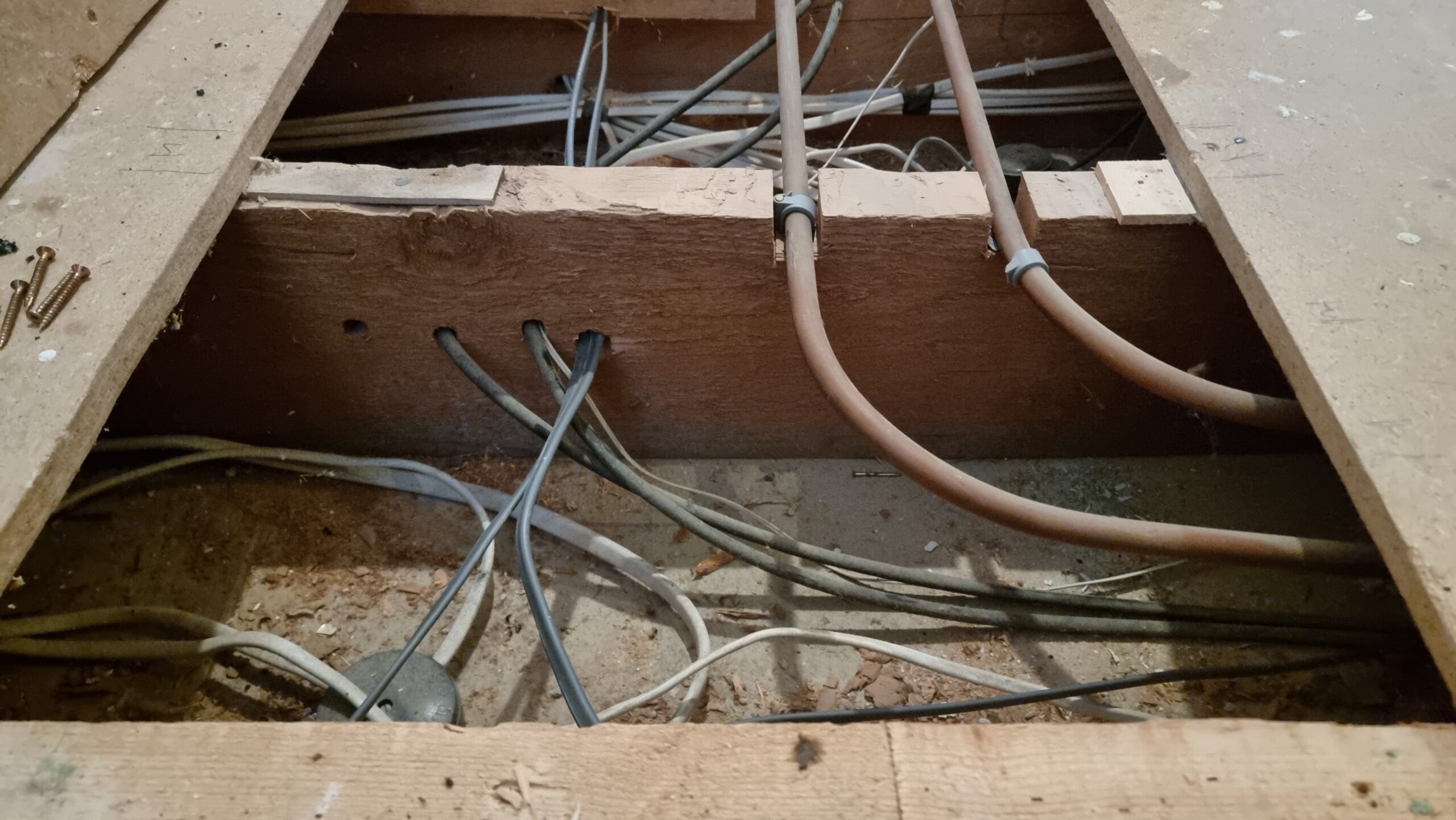 Full image of Lifted floor showing central heating pipes and a tangle of electrical cables.