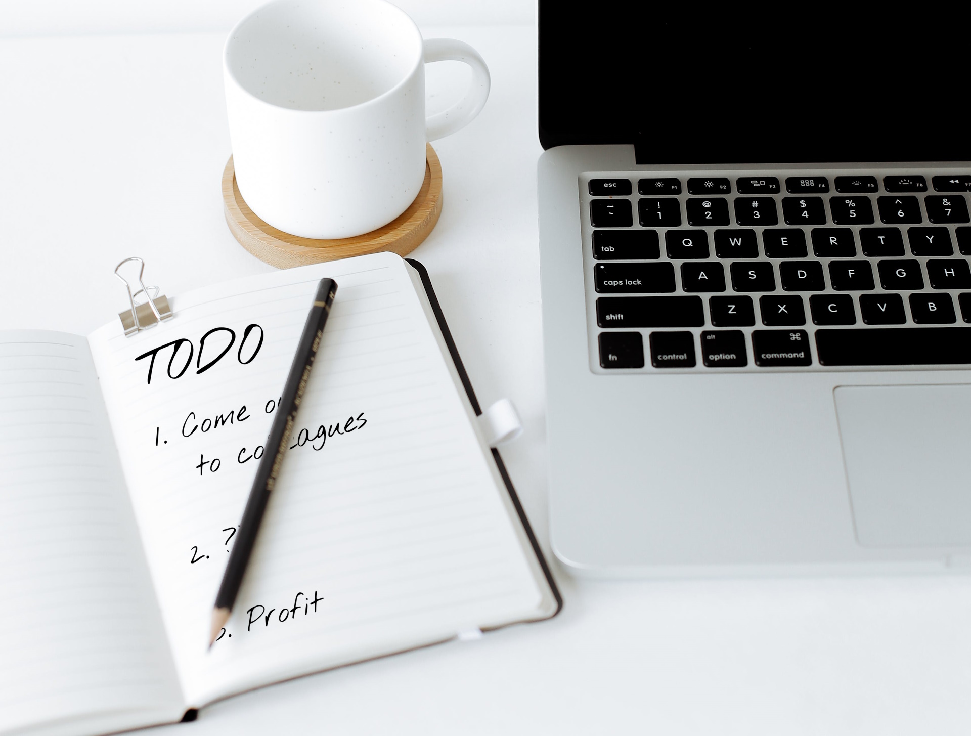 Full image of Laptop and mug alongside a notebook and pencil. In the notebook is written "TODO: 1. Come out to colleagues. 2. ???. 3. Profit."
