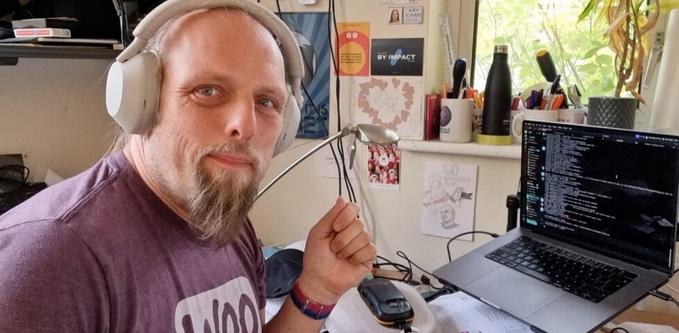 Dead, wearing headphones, smiles in front of his work laptop.