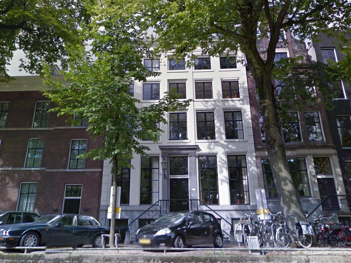Full image of Modern photo, taken from the canal, showing a tall white building in Amsterdam with large windows on the ground floor and also basement level, and an ornamental window above the front door. Photo from Google Street View.