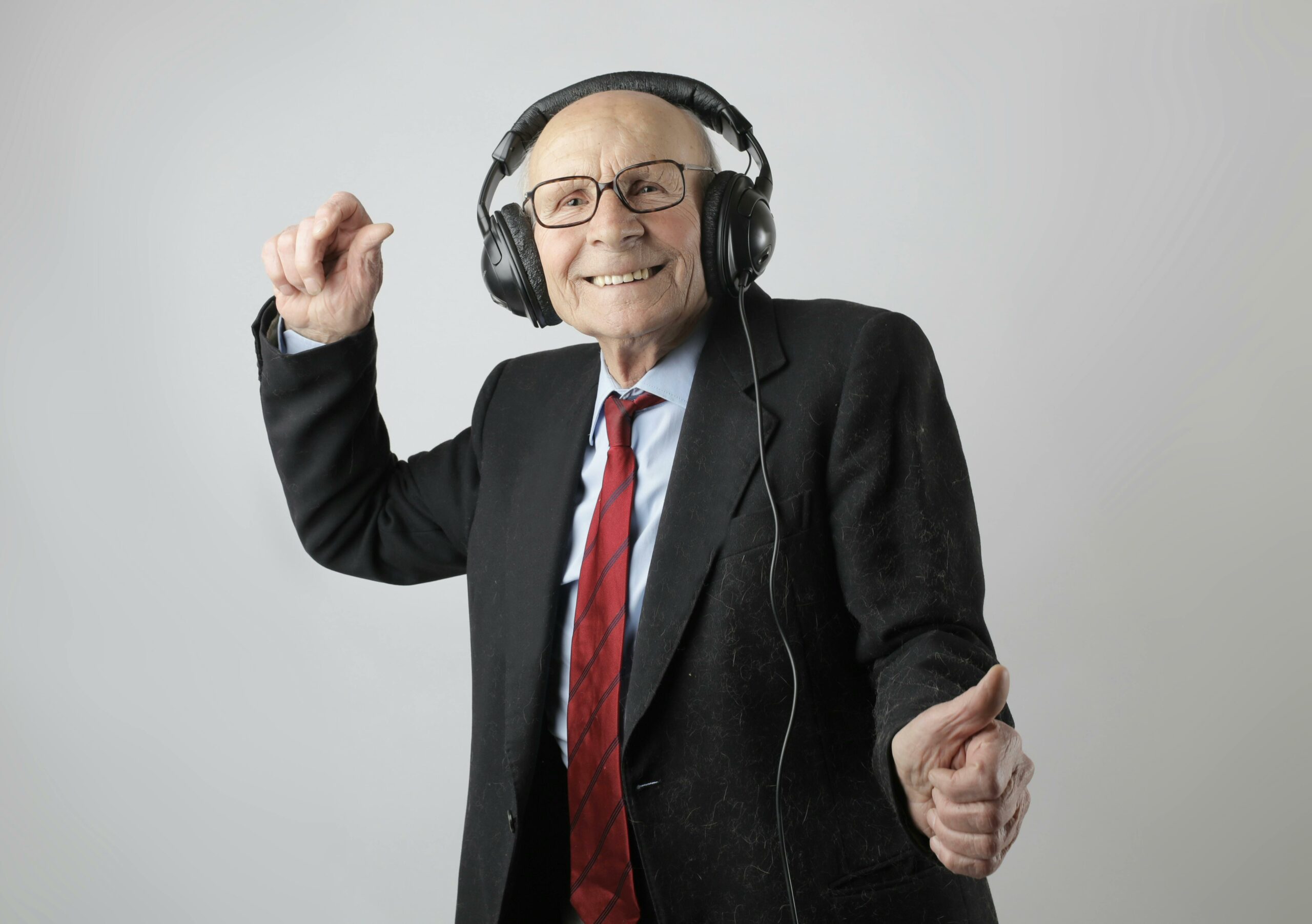 Full image of Cheerful white elderly man listening to music through headphones that are clearly too large for him.