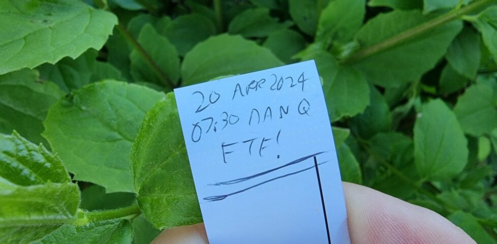 Small geocaching logbook, signed only with "20 Apr 2024 07:30 Dan Q FTF!", against a background of green leaves.