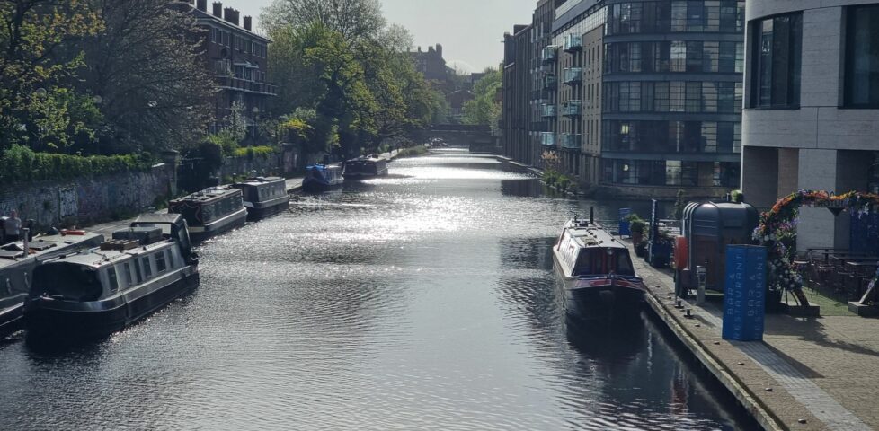 Early morning sun reflects in the water of a peaceful wide canal in central London.