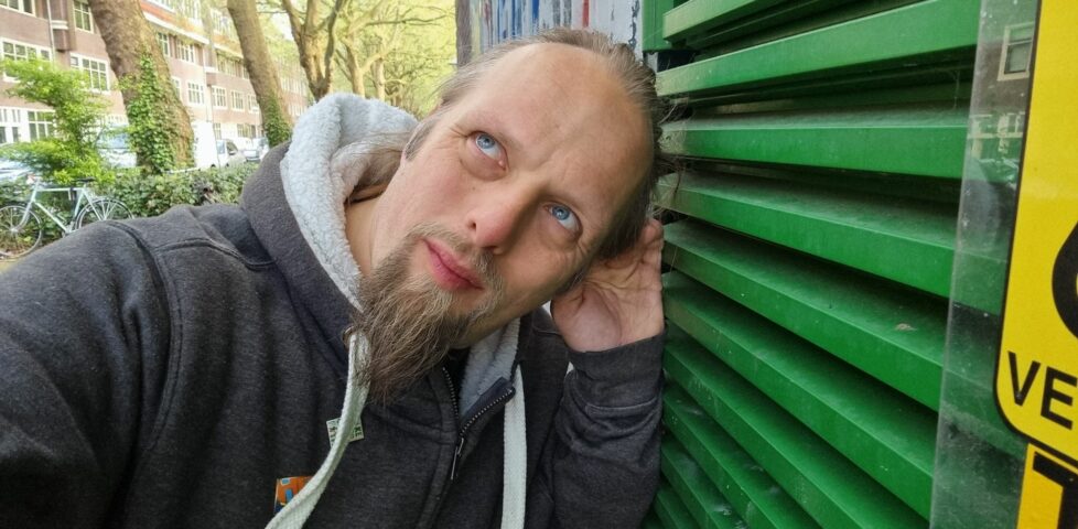 Dan, his hand cupped to his ear, listens closely at the green-painted door of a water pumping station.