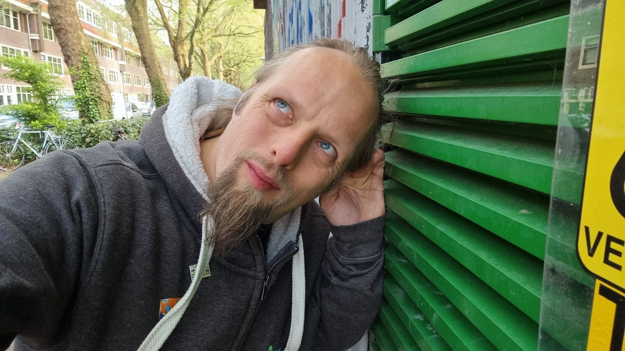 Full image of Dan, his hand cupped to his ear, listens closely at the green-painted door of a water pumping station.