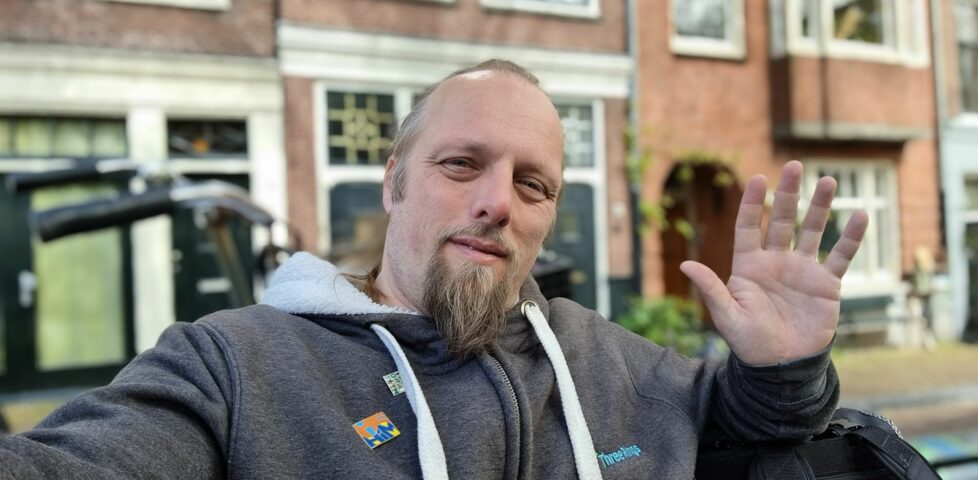 Dan, sat on a bench in Amsterdam, waves.